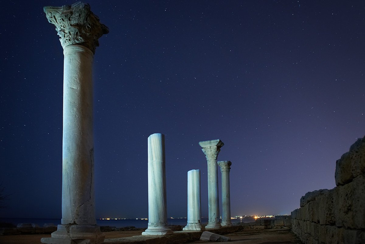 Ruins of ancient city columns under blue night sky with moon