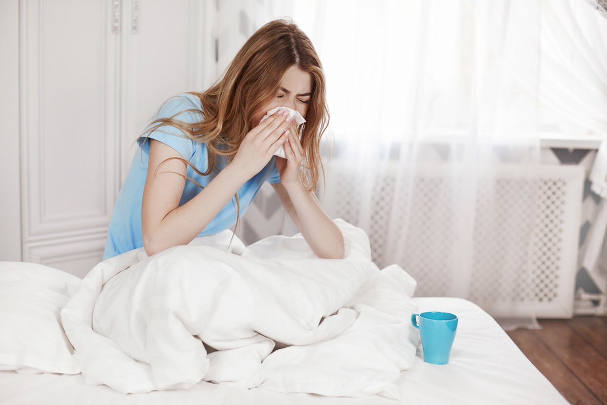 A young sick girl is sitting under a blanket on the bed example image 1