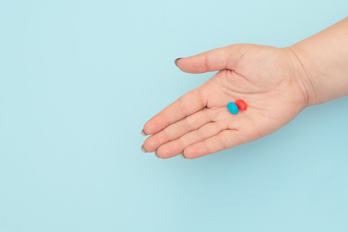 Red and blue pills on female hands on blue background. example image 1