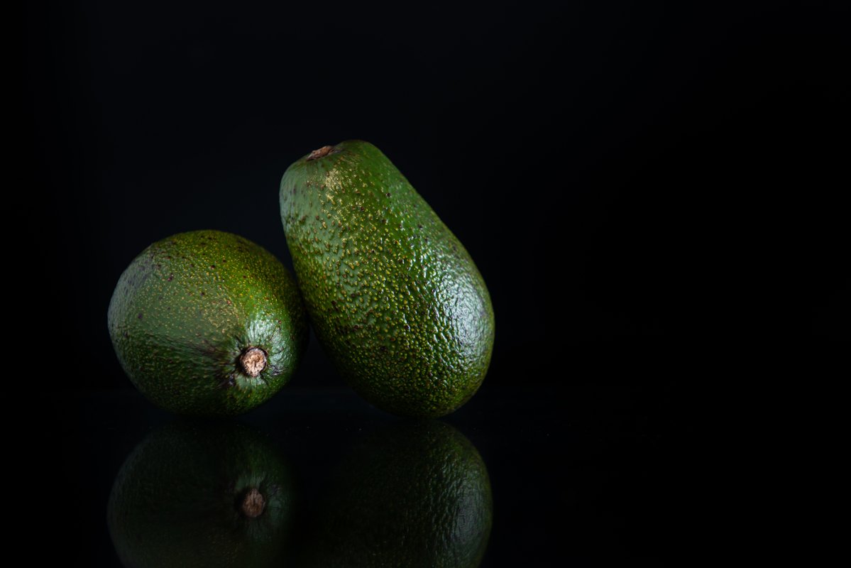 two whole avocados with reflection and copy space on a black example image 1