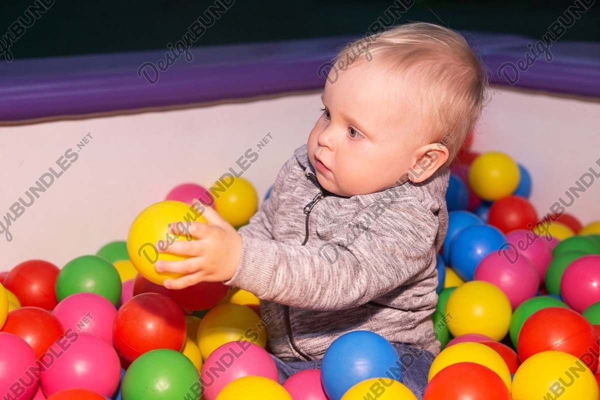 Photo of a baby boy plays with colorful balls in playground example image 1