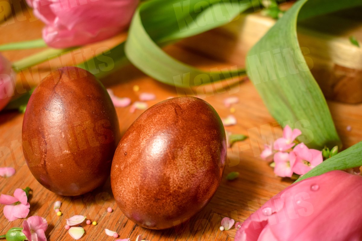 2 Easter eggs on a wooden table with pink flowers and petals example image 1