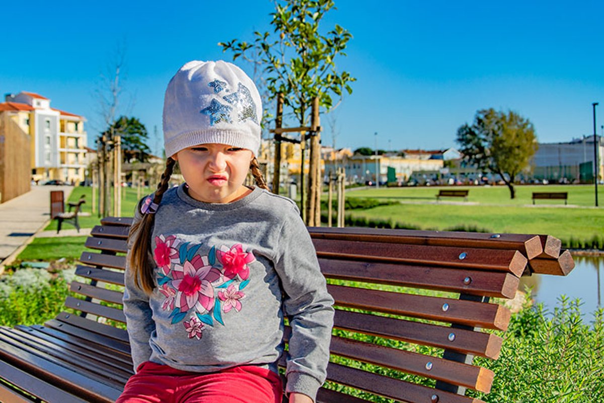 Sad little girl is sitting on a bench in the park. example image 1