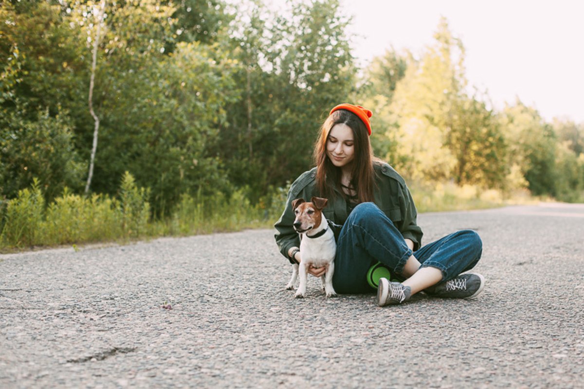 The dog is sitting in front of the girl on the road. example image 1