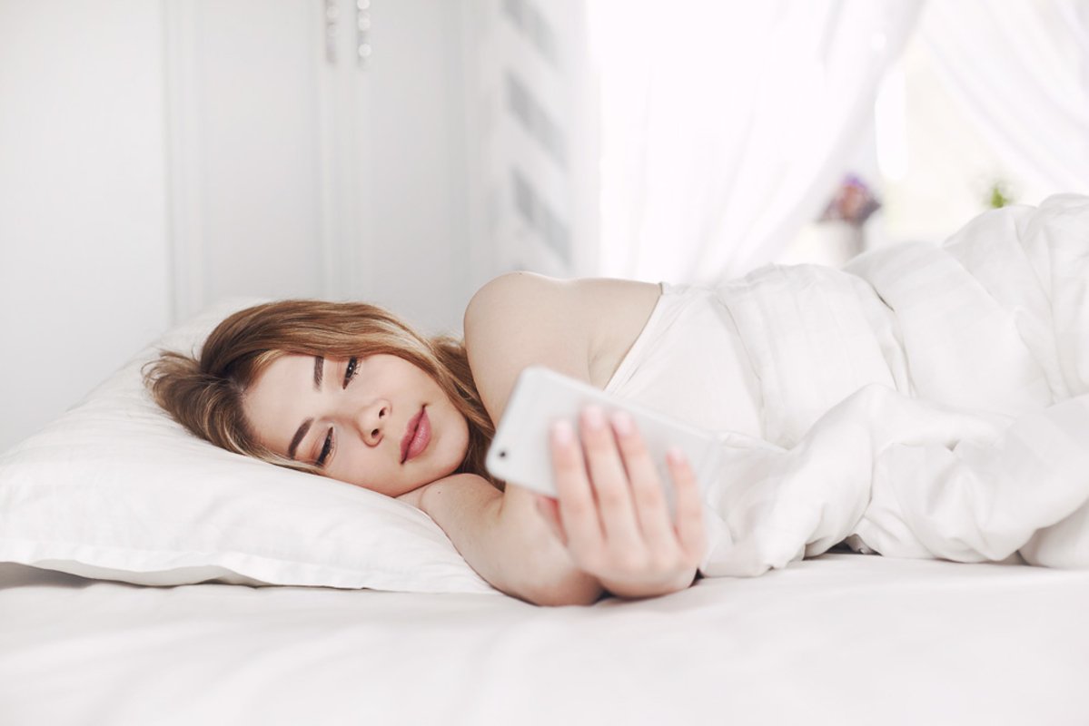 Beautiful young girl looks at the phone while lying example image 1