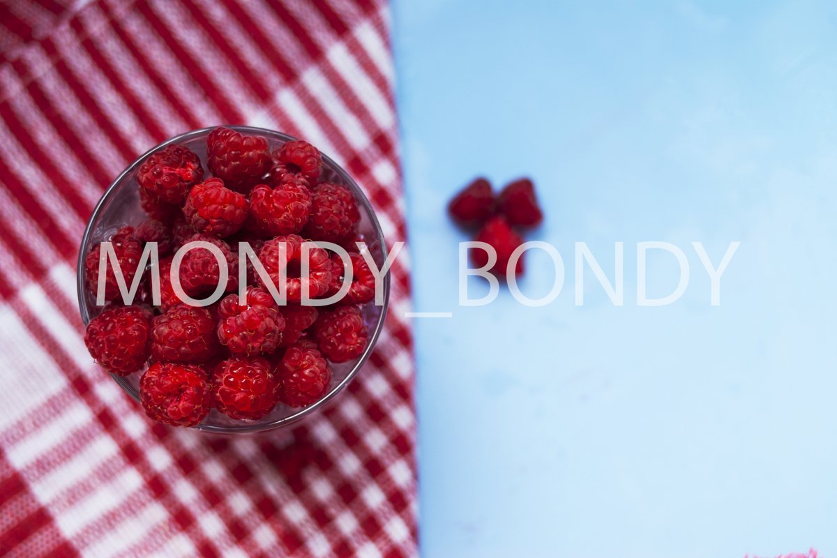 A glass of ripe raspberries with a crumpled plan on a blue b example image 1