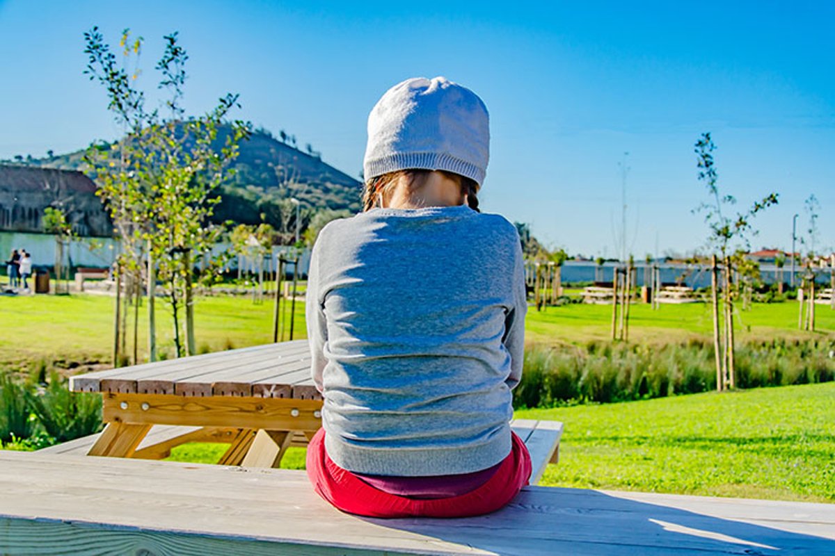 Sad little girl is sitting on a bench in the park. example image 1