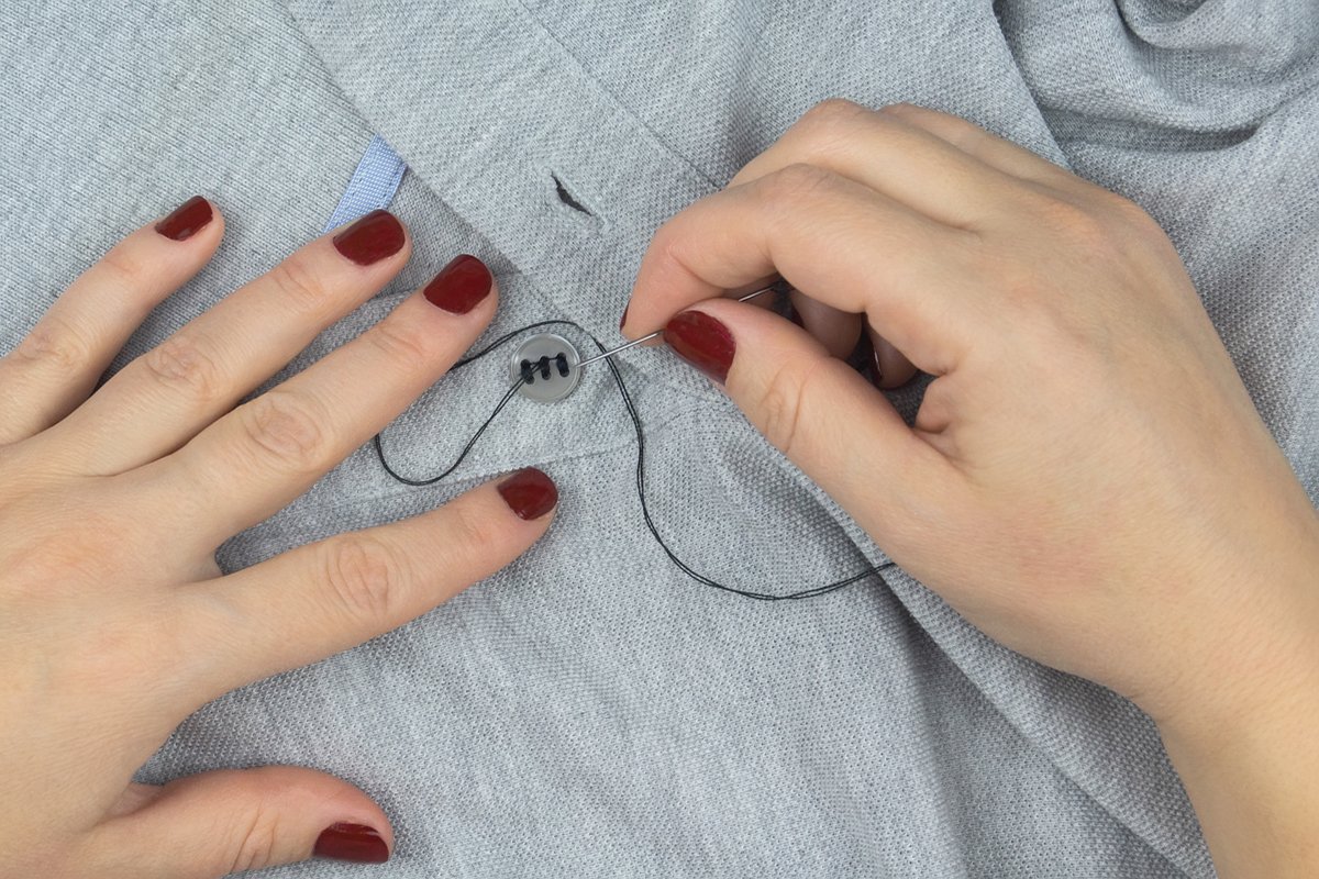 a girl with a needle in her hands sews a button to a shirt example image 1