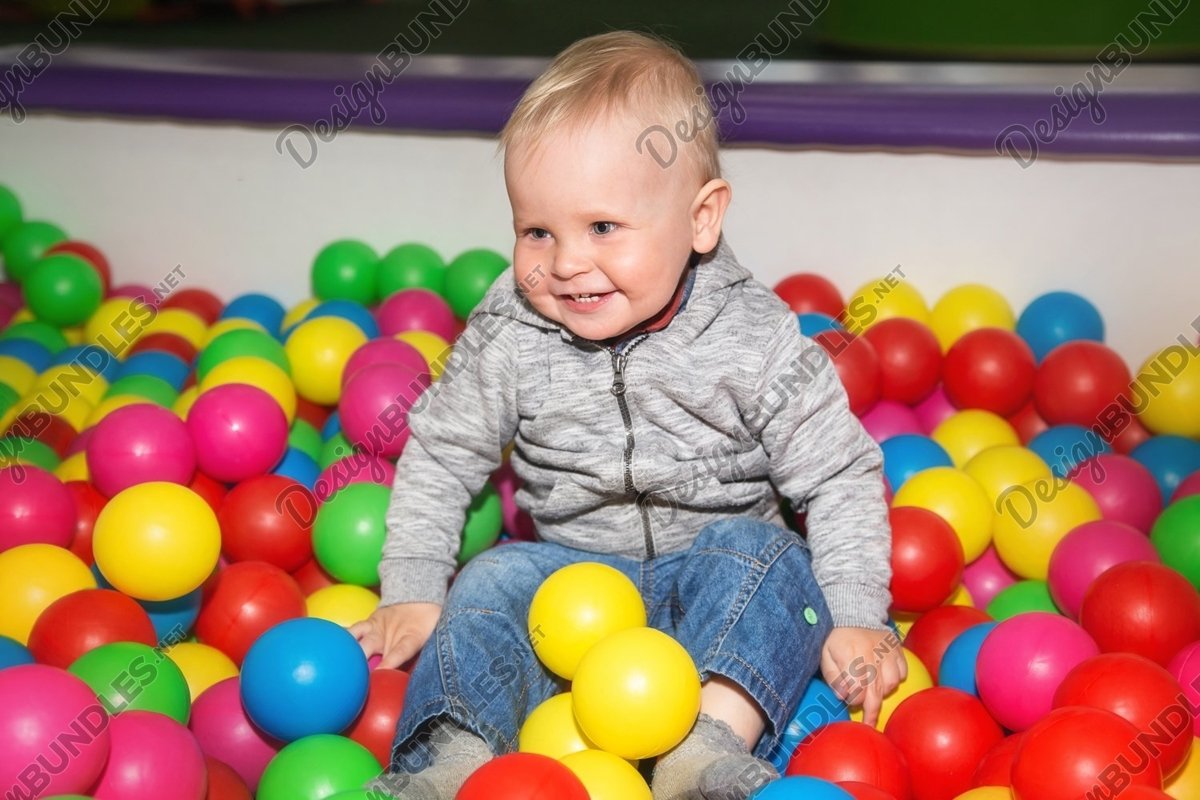 Smiley baby boy plays with colorful balls in playground example image 1