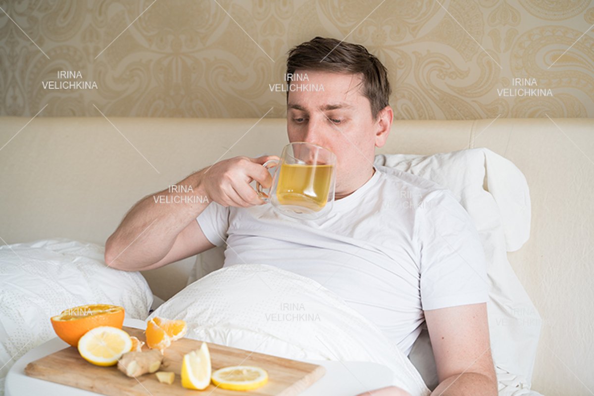 Sick man in bed. Cup of flu drugs. Tea, orange,lemon,ginger example image 1