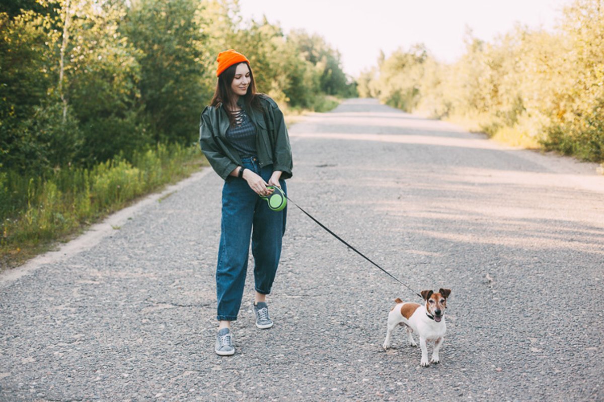 A girl in a green jacket and an orange hat walks with a dog example image 1