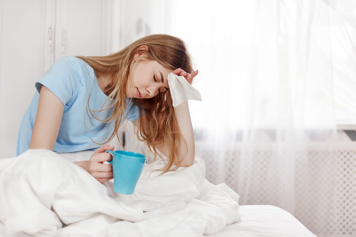 A sick girl with a headache is sitting under a blanket example image 1