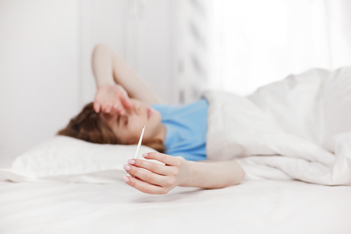 A young girl is sitting on the bed and holding a thermometer example image 1
