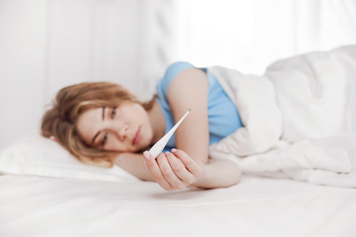 A young girl is sitting on the bed and holding a thermometer example image 1