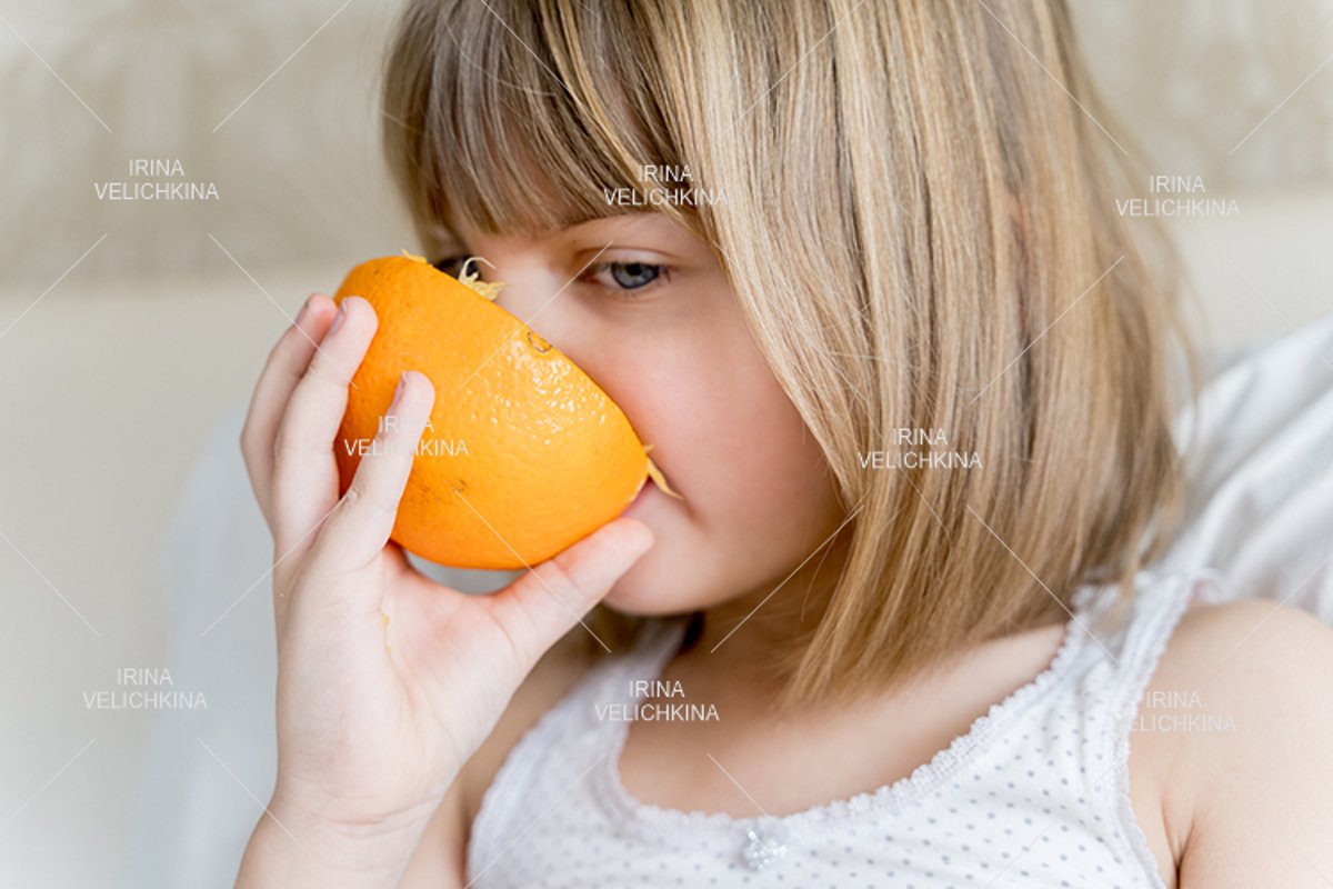 Sick girl in bed. Eating big orange in hands example image 1
