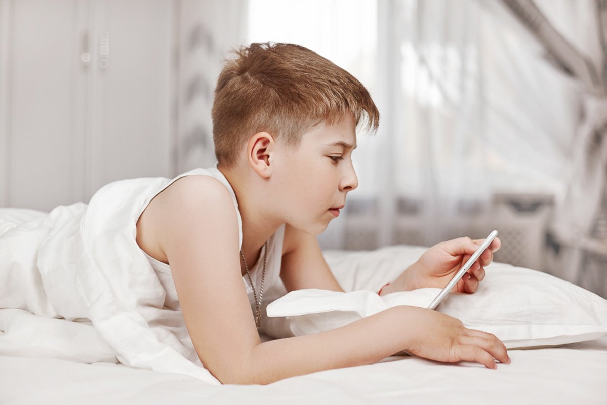 Teen boy with lies on the bed and looks at the phone. example image 1