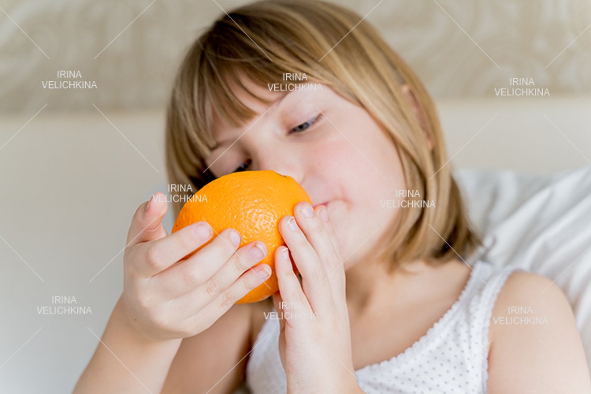 Sick girl in bed. Eating big orange in hands example image 1
