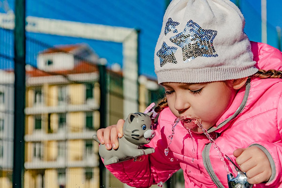 A pre-school girl drinks from a drinking fountain in a park. example image 1