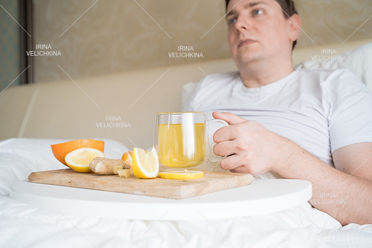 Sick man in bed. Cup of flu drugs. Tea, orange,lemon,ginger example image 1