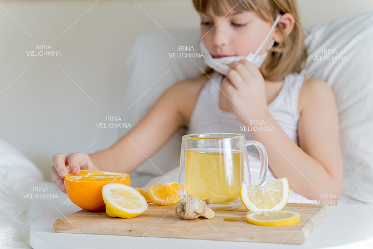 Sick girl in bed. Face mask.Cup of tea, orange,lemon,ginger example image 1