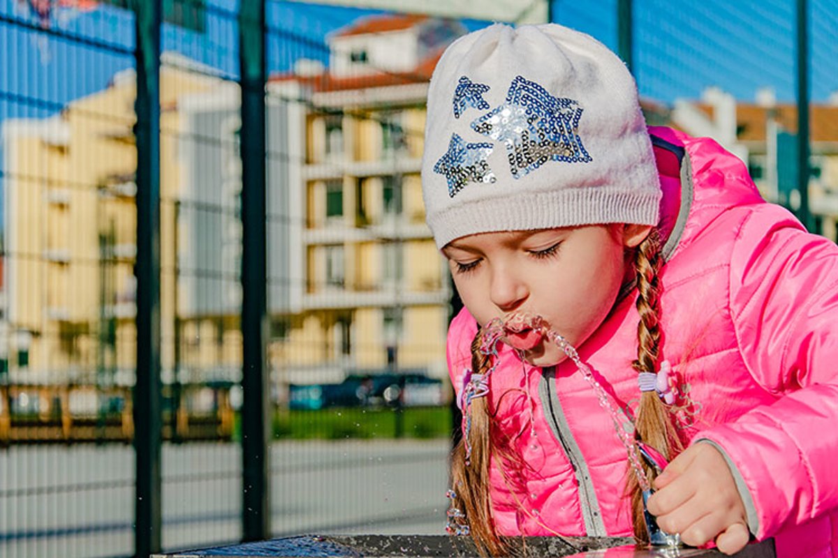 A pre-school girl drinks from a drinking fountain in a park. example image 1