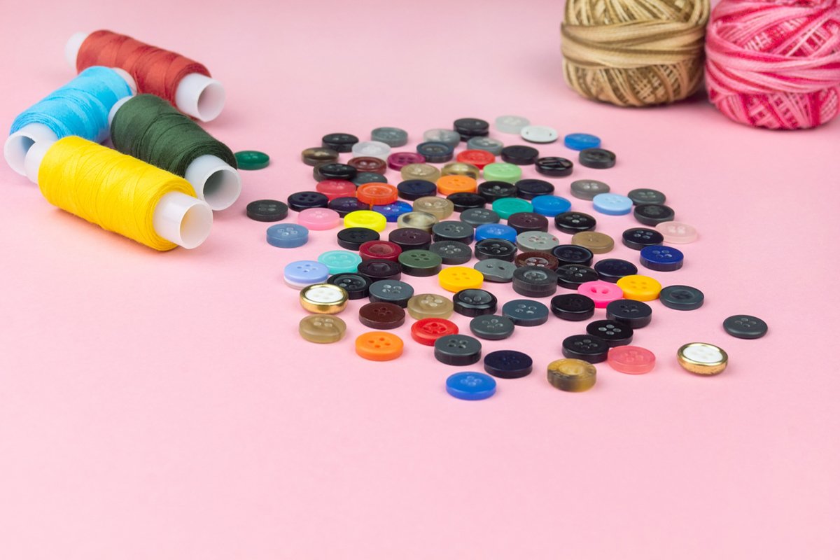 Multicolored threads and buttons on a pink background. example image 1