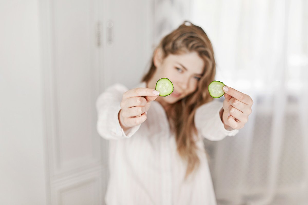 A charming young girl makes a face mask from a cucumber. example image 1