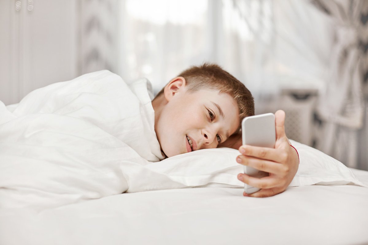 Teen boy with lies on the bed and looks at the phone. example image 1