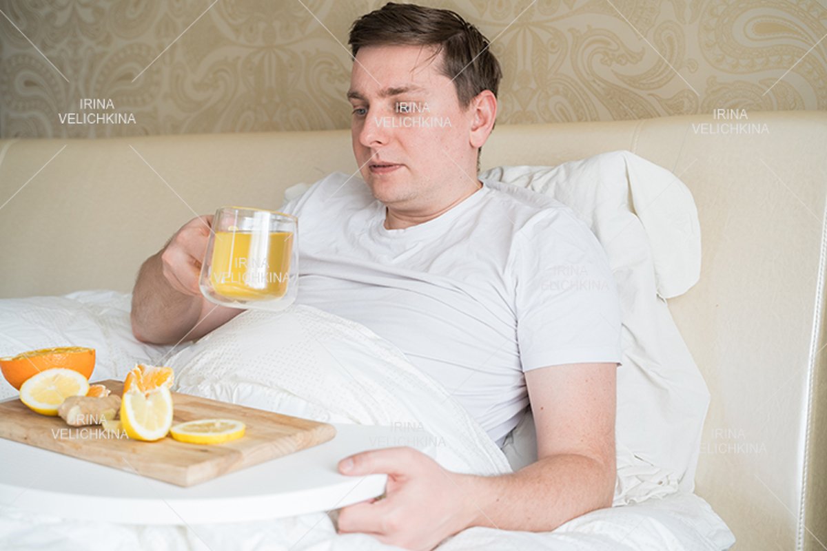 Sick man in bed. Cup of flu drugs. Tea, orange,lemon,ginger example image 1
