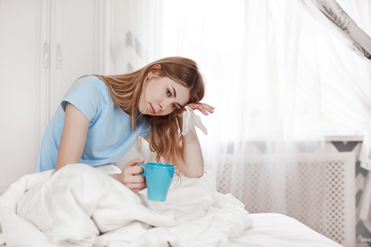 A sick girl with a headache is sitting under a blanket example image 1