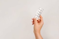 Hand holding medicine pills on a light gray background Product Image 1