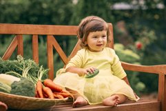 A child sits on a bench next to a basket of vegetables Product Image 1