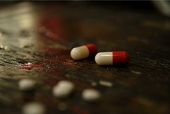 Red and white pills lying on wooden tabletop Product Image 1