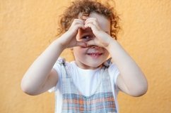 child girl making heart-shape gesture on bright orange Product Image 1