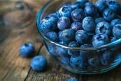 Freshly washed blueberries overflowing in glass bowl on rust Product Image 1