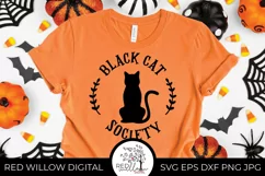 Simple black cat design on an orange t-shirt surrounded by halloween decorations.