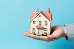 Real estate agent holding house model at blue background. Ge Product Image 1
