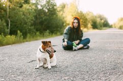 The dog is sitting in front of the girl on the road. Product Image 1