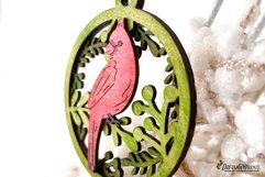 A beautiful Christmas ornament with cardinal and branches behind it.