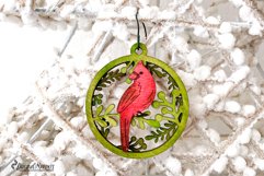 A beautiful Christmas ornament with cardinal and branches behind it.