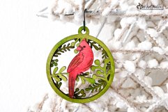 A beautiful Christmas ornament with cardinal and branches behind it.