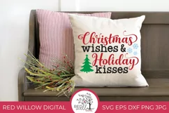 Christmas saying displayed in red black and green with snowflakes and a Christmas tree. It is displayed on a natural colored throw pillow with some christmas decor surrounding it.