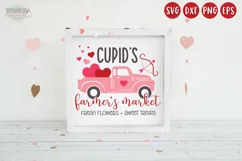 Cupids Farmers Market text with a pink vintage truck filled with hearts on a white sign with a white frame