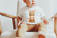 Cute baby bunny in hunting camo hat holding Easter eggs in woven basket. Neutral earthy tones with pastel eggs for toddler Easter shirt design.