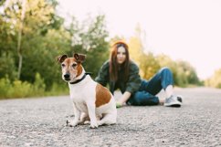 The dog is sitting in front of the girl on the road. Product Image 1