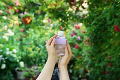 Woman&#039;s hands hold face tonic bottle on a flowering natural Product Image 1
