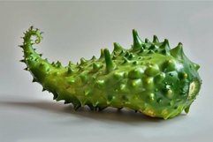 Green spiky kiwano melon is laying on a white surface Product Image 1