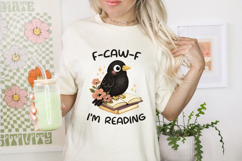 Bookish humor graphic showing a crow perched on an open book with cozy floral details and bold “I’m Reading” text, designed for cozy reader vibes and gifts.
