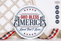 God Bless America written in a fancy old style font with red and blue stars shown on a white round sign