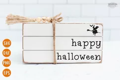 Happy Halloween text with a witch riding a broom shown on a white wooden book stack